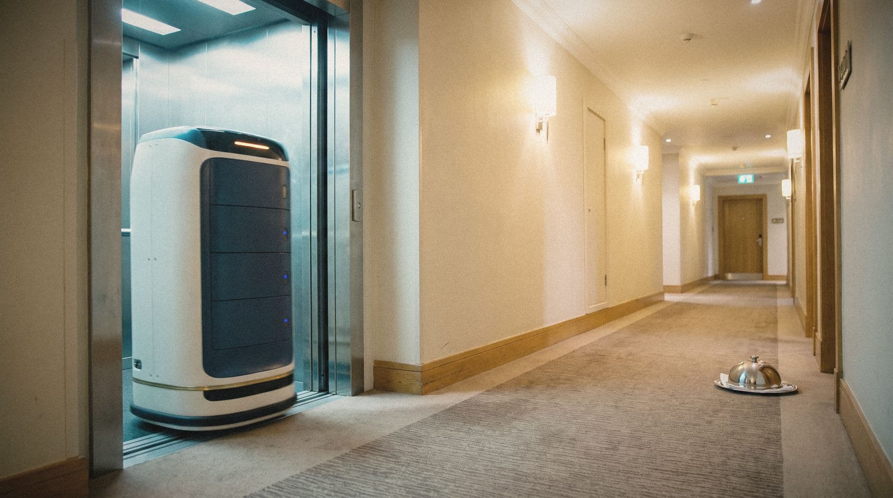 A Monadex Courier robot rolling out of a lift into a hotel corridor at night
